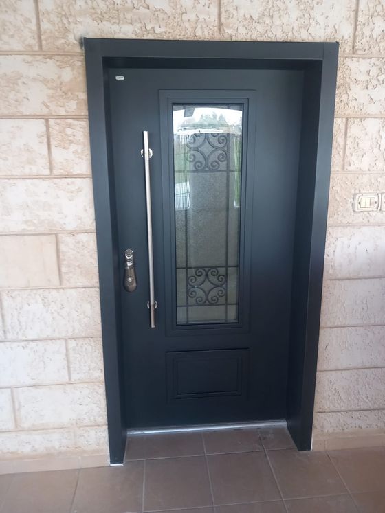 דלת כניסה כהה עם חלונית זכוכית מעוטרת וידית ארוכה